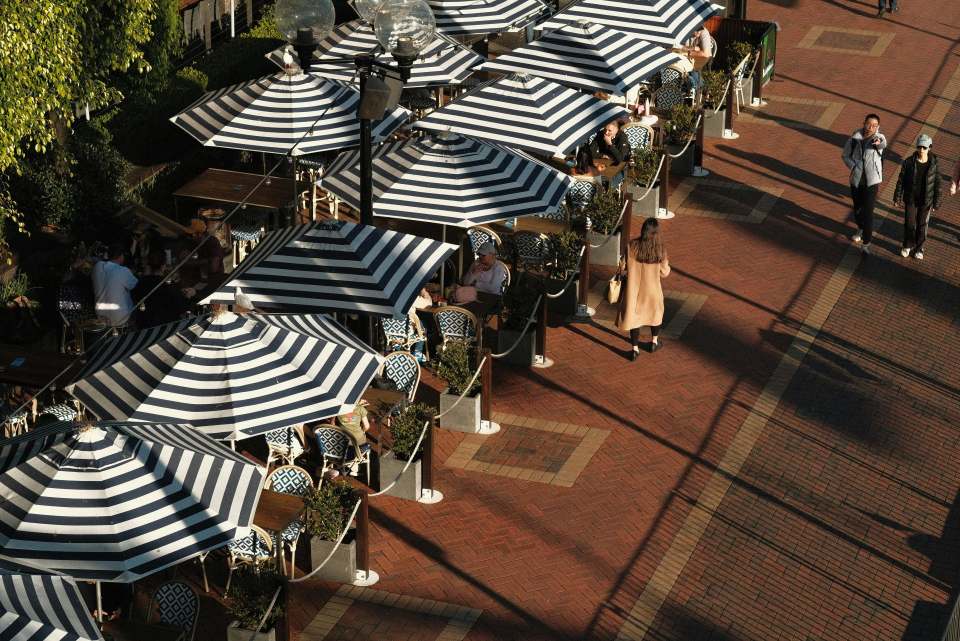 A group of people sitting under umbrellas on a sidewalk